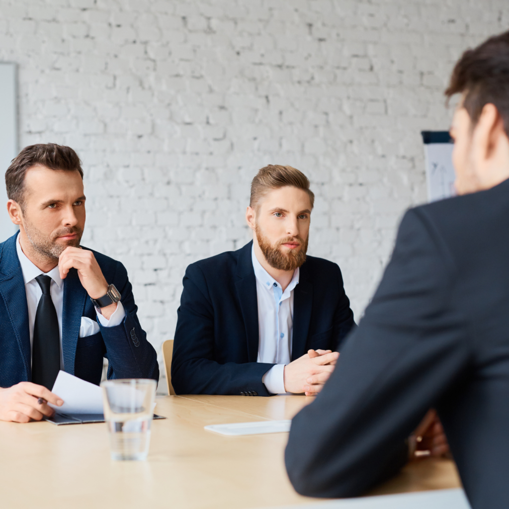 Three business professionals conducting a job interview with a candidate at a wooden table in an office setting.