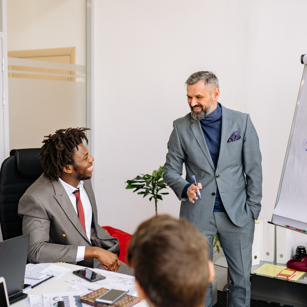 Two professional businessmen in suits engaged in discussion during a food industry meeting, with documents and office supplies visible on the desk.