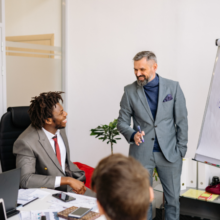 Two professional businessmen in suits engaged in discussion during a food industry meeting, with documents and office supplies visible on the desk.