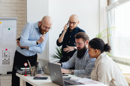 Four professionals collaborating around a laptop during a business meeting, discussing strategy and solutions in a modern office environment.