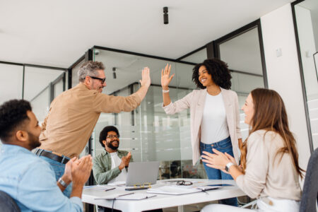 A diverse team of professionals giving high-fives in a modern office, celebrating a successful business achievement or milestone.
